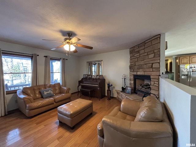 living area with ceiling fan, a stone fireplace, and light wood-type flooring