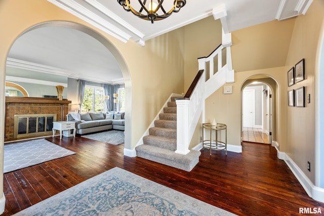 entryway featuring an inviting chandelier, ornamental molding, dark hardwood / wood-style floors, and a brick fireplace