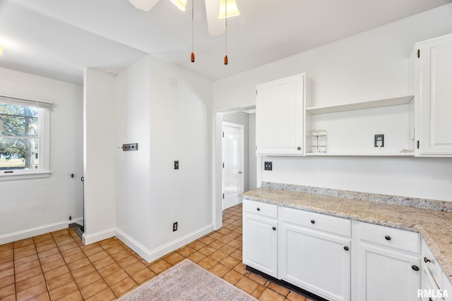 kitchen with white cabinetry, ceiling fan, light tile patterned flooring, and light stone counters