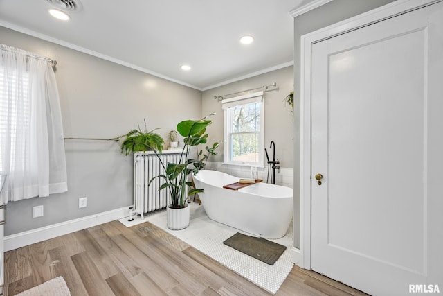 bathroom with a tub to relax in, hardwood / wood-style flooring, radiator heating unit, and ornamental molding