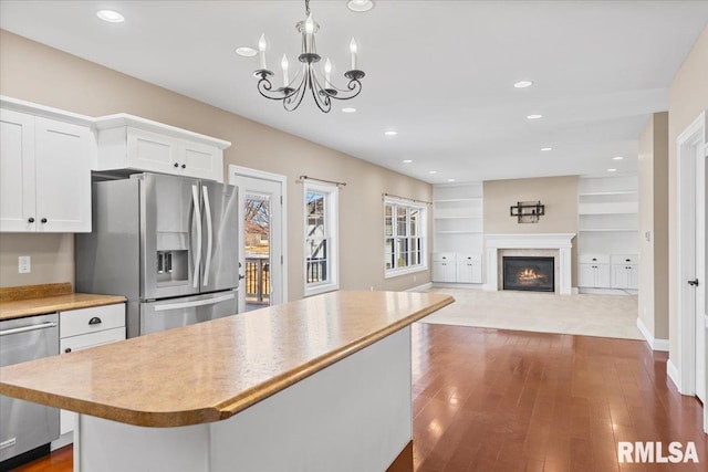 kitchen with a kitchen island, appliances with stainless steel finishes, pendant lighting, white cabinetry, and dark wood-type flooring