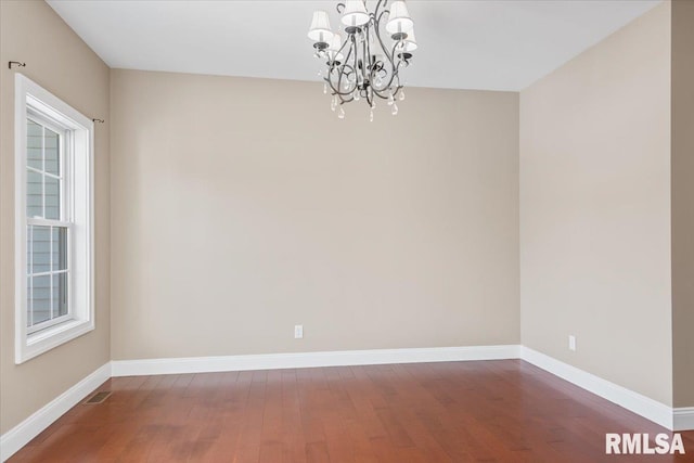 spare room with hardwood / wood-style flooring and an inviting chandelier