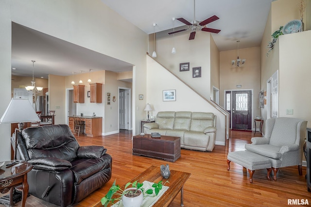 living room with ceiling fan with notable chandelier, a towering ceiling, and light wood-type flooring