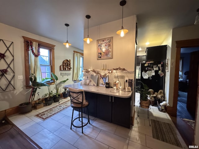 kitchen with black fridge, a breakfast bar area, hanging light fixtures, and light tile patterned floors