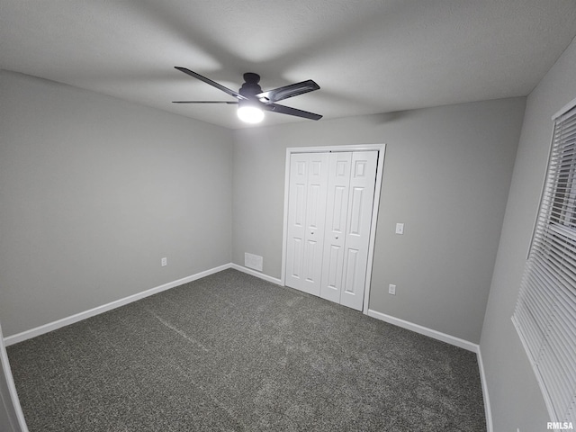 unfurnished bedroom with dark colored carpet, ceiling fan, and a closet