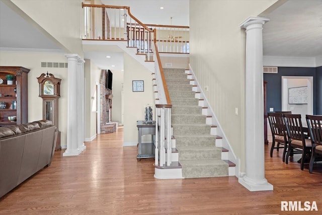 stairs with ornamental molding, wood-type flooring, decorative columns, and a high ceiling