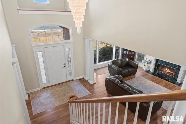 foyer entrance with ornate columns, wood-type flooring, a chandelier, a high ceiling, and a premium fireplace