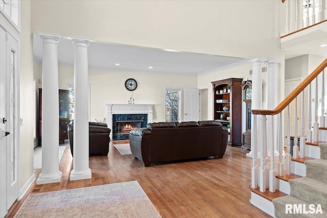 living room with ornate columns, a fireplace, wood-type flooring, a high ceiling, and crown molding