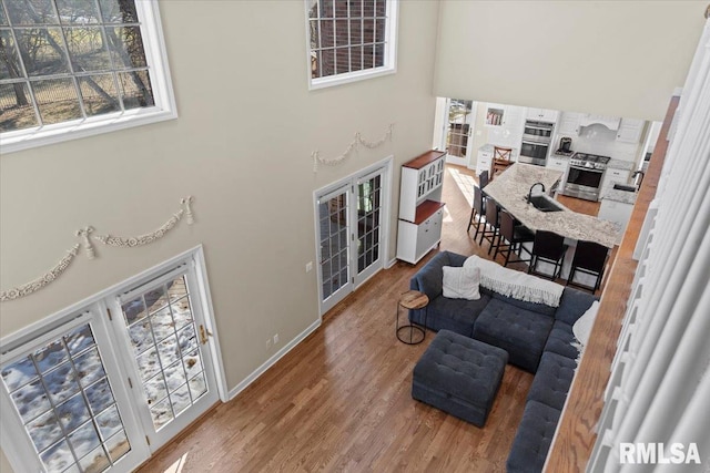 living room with french doors, a towering ceiling, sink, and hardwood / wood-style floors