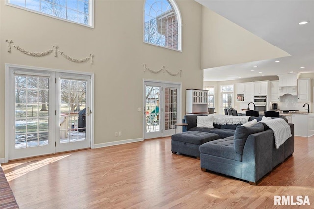 living room with a towering ceiling, plenty of natural light, french doors, and light wood-type flooring