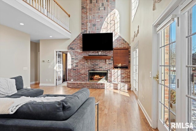 living room featuring hardwood / wood-style flooring, a towering ceiling, and a brick fireplace