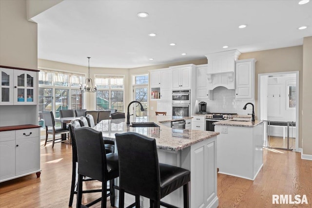 kitchen featuring pendant lighting, sink, appliances with stainless steel finishes, a kitchen island with sink, and white cabinets