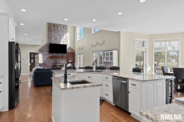 kitchen with white cabinetry, dishwasher, black fridge, and an island with sink