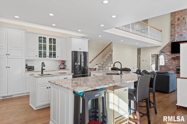 kitchen with black refrigerator with ice dispenser, sink, an island with sink, and white cabinets