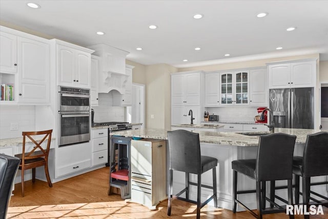 kitchen with sink, appliances with stainless steel finishes, white cabinetry, light stone counters, and an island with sink