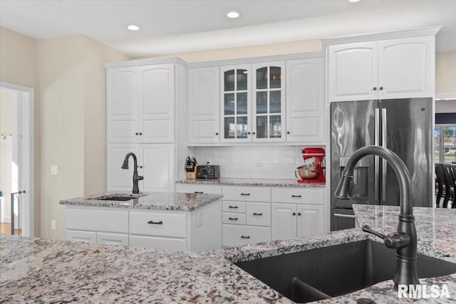 kitchen featuring sink, stainless steel refrigerator with ice dispenser, light stone counters, tasteful backsplash, and white cabinets