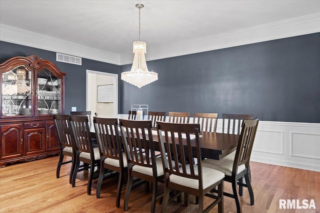 dining area with an inviting chandelier, ornamental molding, and light hardwood / wood-style flooring