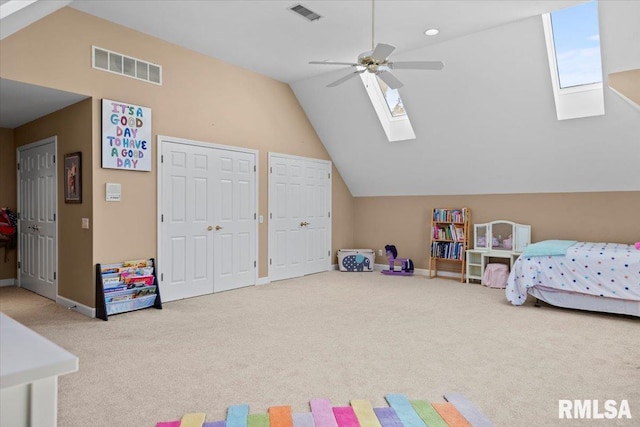 carpeted bedroom featuring ceiling fan, vaulted ceiling with skylight, and multiple closets