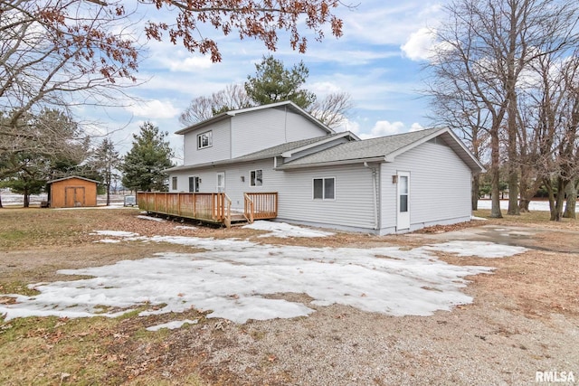 snow covered rear of property featuring a wooden deck and a shed