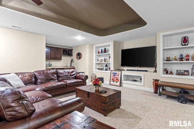 carpeted living room featuring built in shelves and a tray ceiling