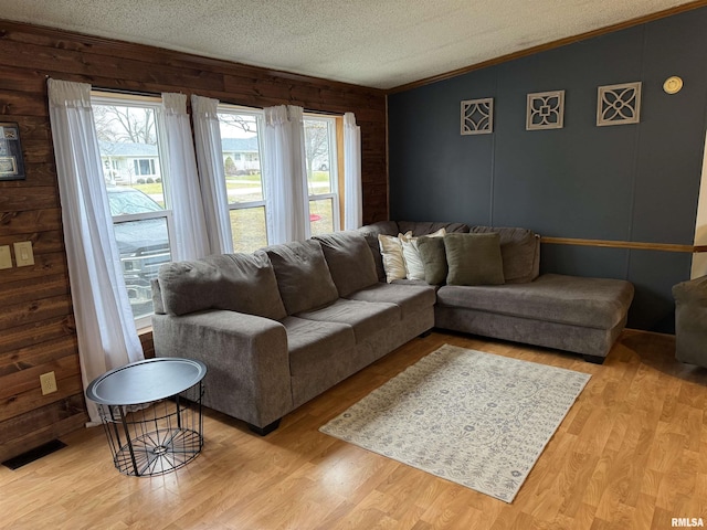 living room with vaulted ceiling, wood walls, a textured ceiling, and light hardwood / wood-style flooring