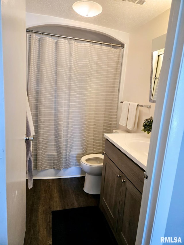 full bathroom with hardwood / wood-style floors, vanity, toilet, shower / bathtub combination with curtain, and a textured ceiling