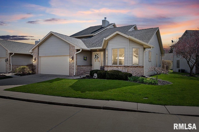 view of front of property featuring an attached garage, brick siding, a yard, driveway, and roof with shingles