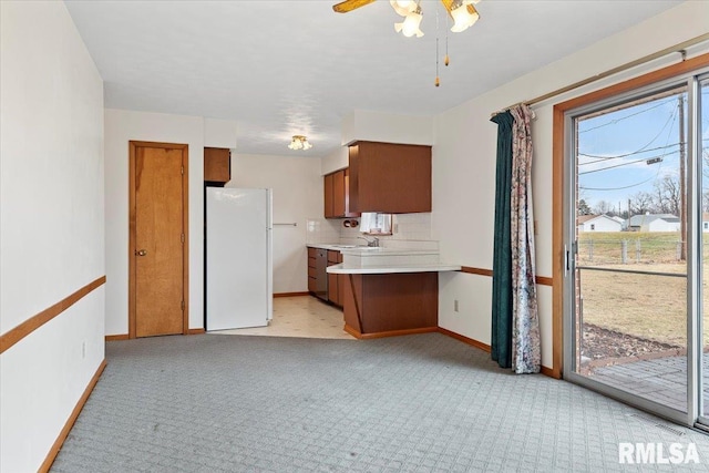 kitchen with sink, white refrigerator, kitchen peninsula, light colored carpet, and backsplash