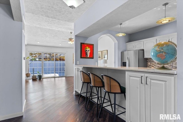 kitchen with dark wood-type flooring, stainless steel fridge, a breakfast bar area, white cabinetry, and kitchen peninsula