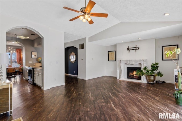 living room with dark wood-type flooring, a premium fireplace, ceiling fan with notable chandelier, and vaulted ceiling