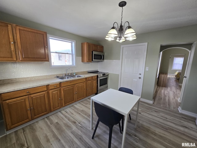 kitchen with sink, tasteful backsplash, hanging light fixtures, light wood-type flooring, and appliances with stainless steel finishes