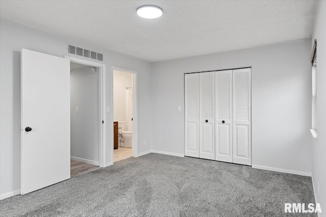 unfurnished bedroom with a closet, connected bathroom, carpet floors, and a textured ceiling