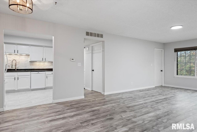 unfurnished living room with sink, a textured ceiling, and light wood-type flooring