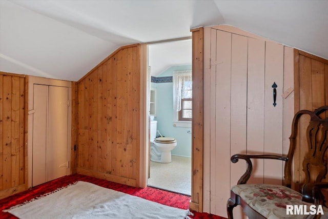 bedroom featuring ensuite bath, wooden walls, and vaulted ceiling