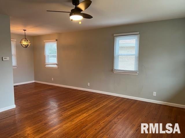 empty room featuring dark wood-type flooring and ceiling fan with notable chandelier