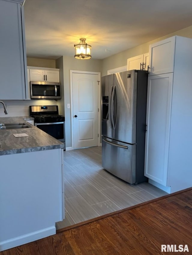 kitchen featuring sink, appliances with stainless steel finishes, white cabinetry, decorative light fixtures, and light wood-type flooring