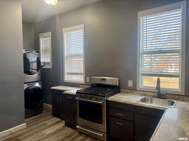 kitchen with sink, stainless steel gas range, stacked washer / drying machine, a wealth of natural light, and wood-type flooring