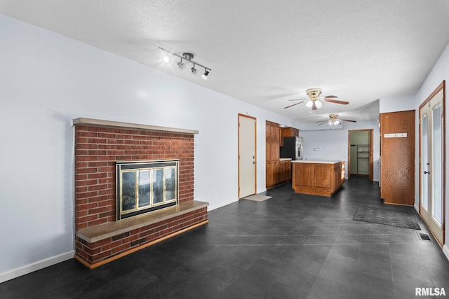 unfurnished living room with ceiling fan, a brick fireplace, and a textured ceiling