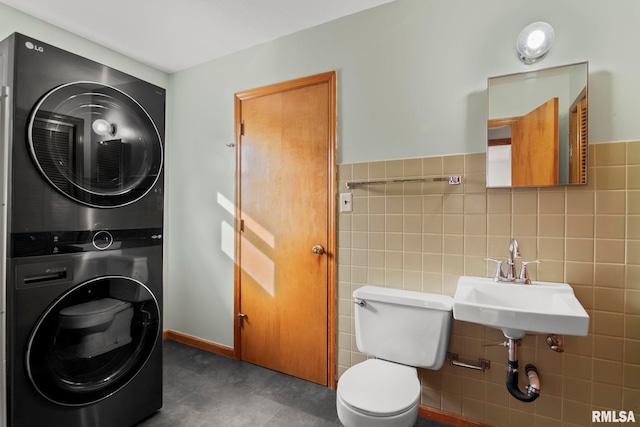 bathroom with stacked washer and dryer, toilet, sink, and tile walls