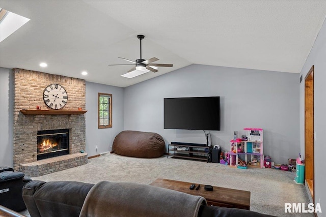 living room featuring ceiling fan, carpet flooring, vaulted ceiling with skylight, and a fireplace