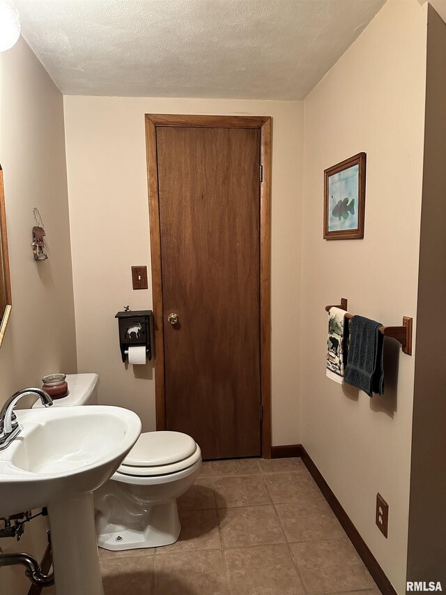 bathroom with a textured ceiling, toilet, baseboards, and tile patterned floors