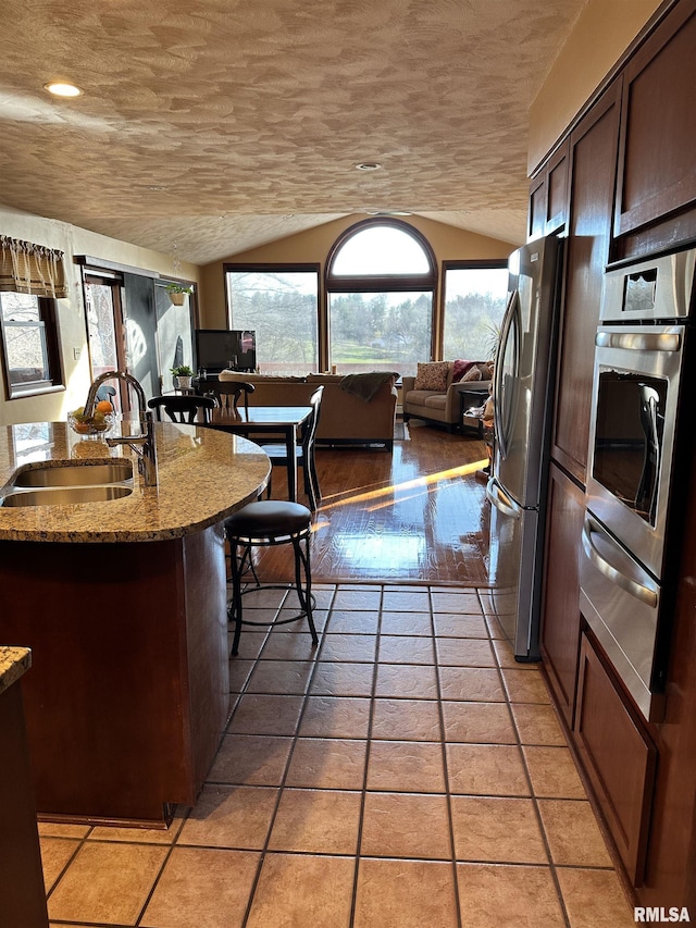 kitchen with light stone counters, lofted ceiling, appliances with stainless steel finishes, and sink