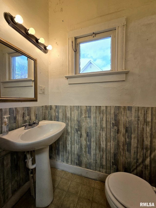 bathroom featuring wood walls, toilet, and a wealth of natural light