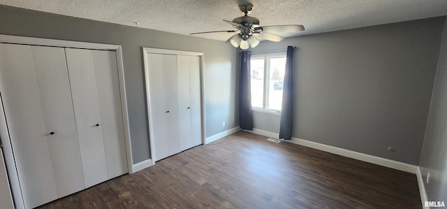 unfurnished bedroom with ceiling fan, dark hardwood / wood-style floors, a textured ceiling, and two closets