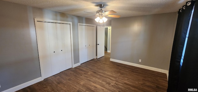 unfurnished bedroom featuring ceiling fan, two closets, dark hardwood / wood-style floors, and a textured ceiling