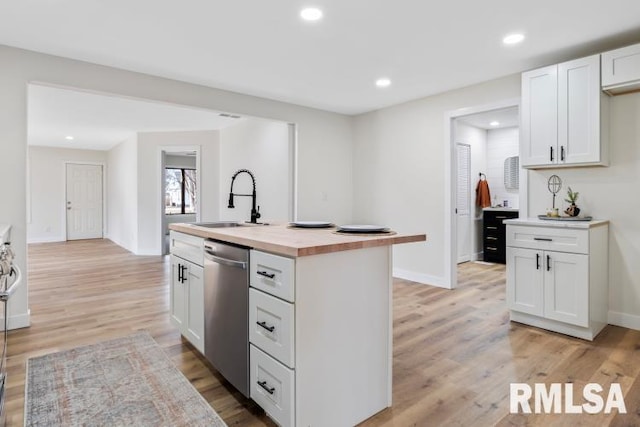 kitchen with butcher block countertops, sink, dishwasher, white cabinetry, and a kitchen island with sink