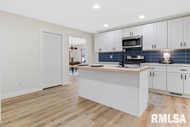 kitchen with sink, white cabinetry, stainless steel appliances, a center island with sink, and decorative backsplash