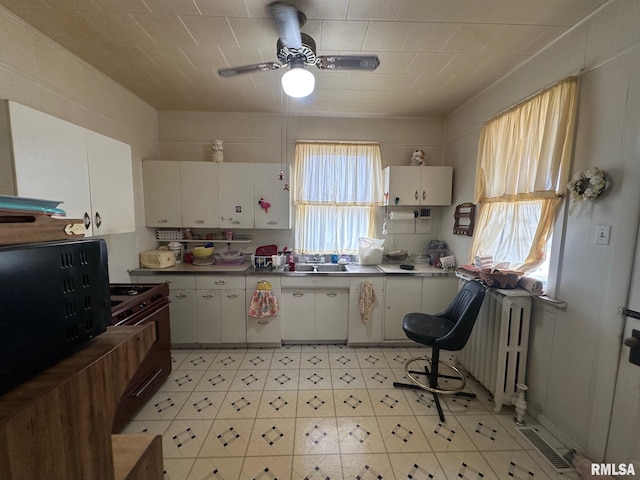 kitchen with radiator heating unit, white cabinets, ceiling fan, and range