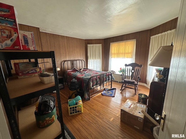 bedroom with wooden walls, radiator, and hardwood / wood-style floors