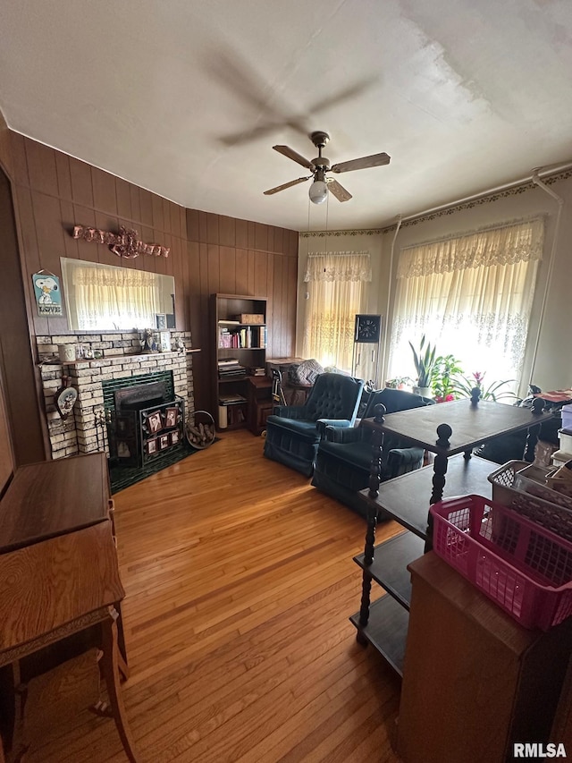 living room featuring hardwood / wood-style flooring, a brick fireplace, ceiling fan, and wood walls